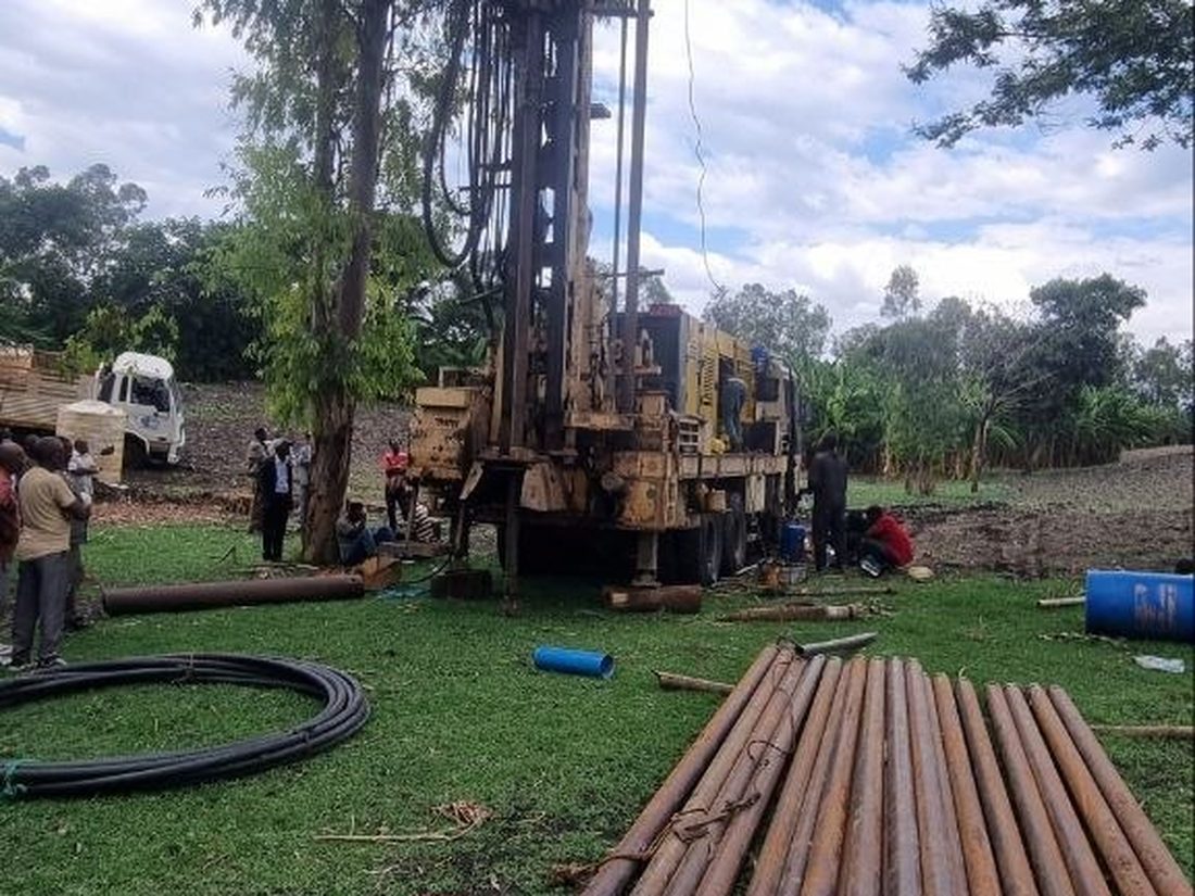 A drilling rig at work among tall trees with drill rods laid out on the ground