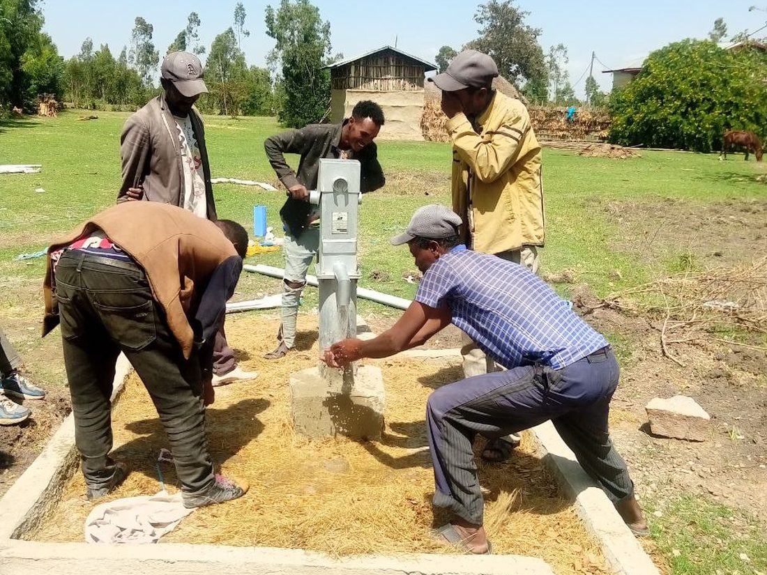 A completed hand pump with a rural community gathered around it, houses behind
