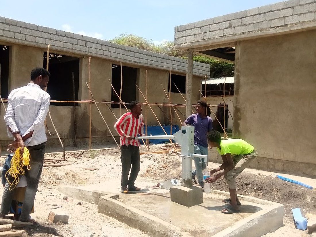 A hand pump at an institutional building under construction, workers testing the pump