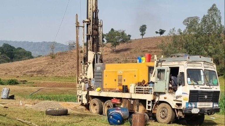 A drilling rig and support truck beside a completed wellhead in an open field
