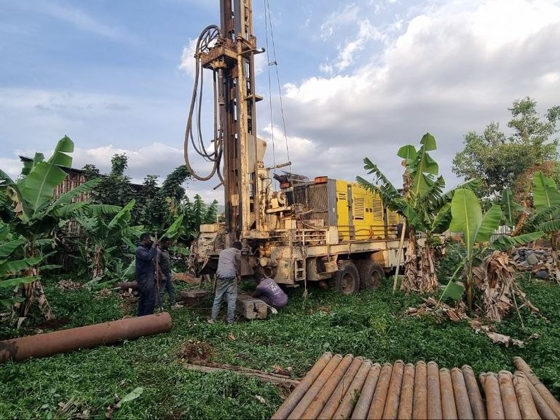 A drilling rig and crew working in a green field with drill rods in the foreground